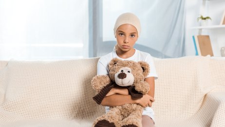 Sykt barn Bildet viser et sykt barn som sitter i en sofa og har en teddybjørn i fanget