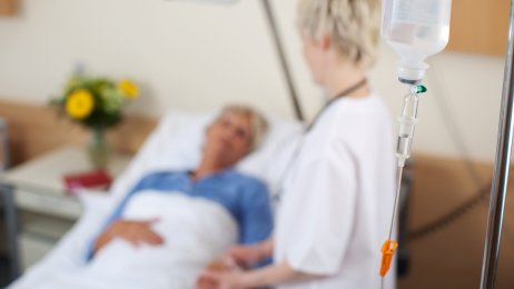Sykepleier og pasient Bildet viser en sykepleier som står ved siden av en sengeliggende pasient