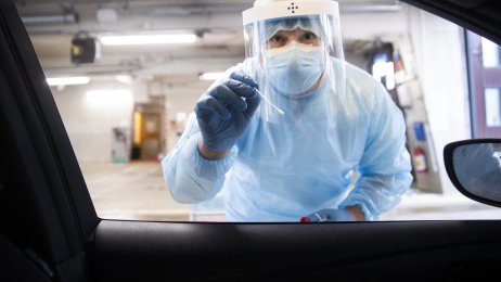 Helsearbeider, koronatest Bildet viser en helsearbeider i smittevernutstyr som holder frem en testpinne.