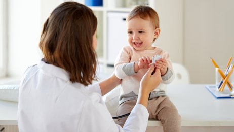 En baby undersøkes av en helsearbeider. En blid baby sitter på et bord og blir undersøkt av en helsearbeider.