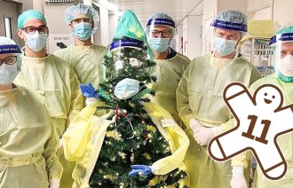 Bildet viser et juletre kledd i smittevernutstyr, omgitt av seks intensivleger.