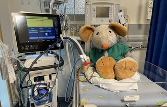 Bildet viser kosedyret Rasmus i en babyseng med respirator ved siden av