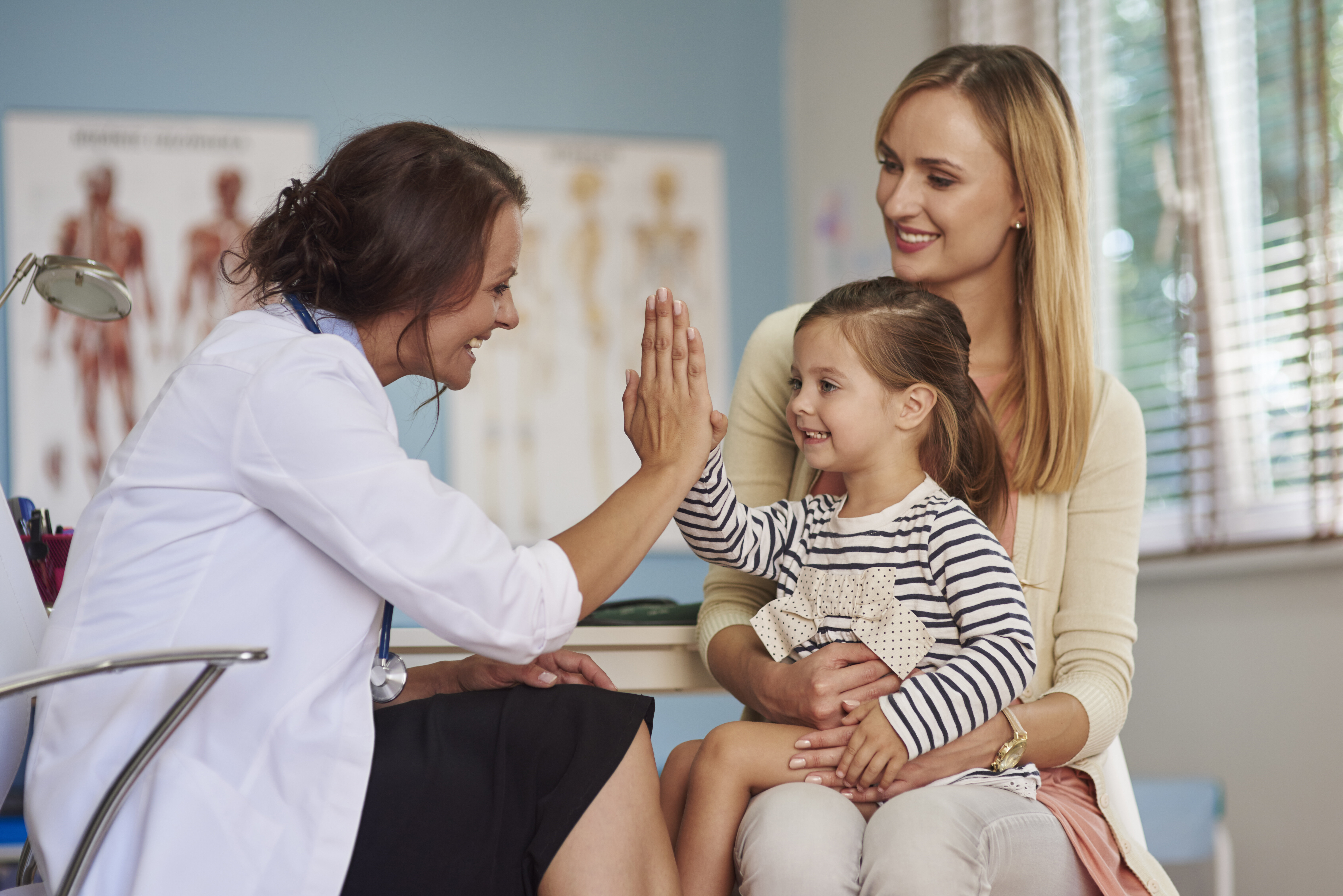 Mor og datter hos helsesykepleieren Bildet viser en liten datter på fanget til mora. Dattera gjør high five med en helsesykepleier som sitter overfor dem