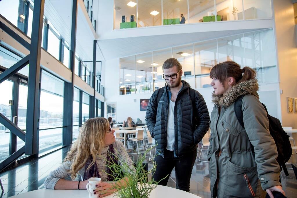 Anette Sagen, sykepleierstudent Bildet viser Anette Sagen som sitter ved et bord i kantinen og snakker med to medstudenter som står.