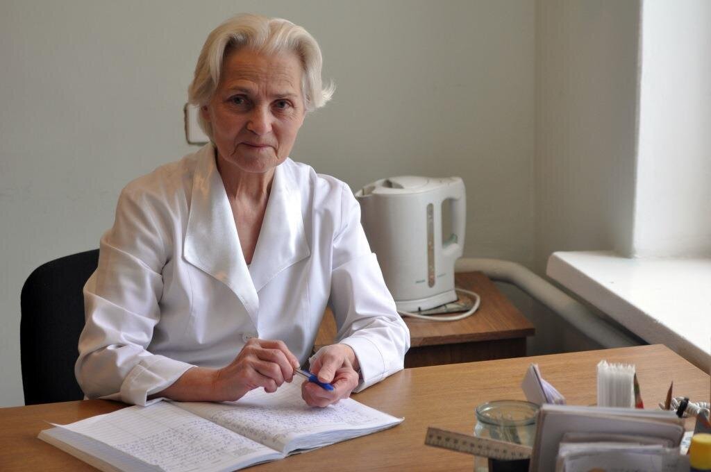 Helseminister Høie ønsker å la sykepleiere og annet helsepersonell beholde autorisasjonen til fylte 80 år. Bildet viser en eldre, kvinnelig helsearbeider bak et skrivebord.