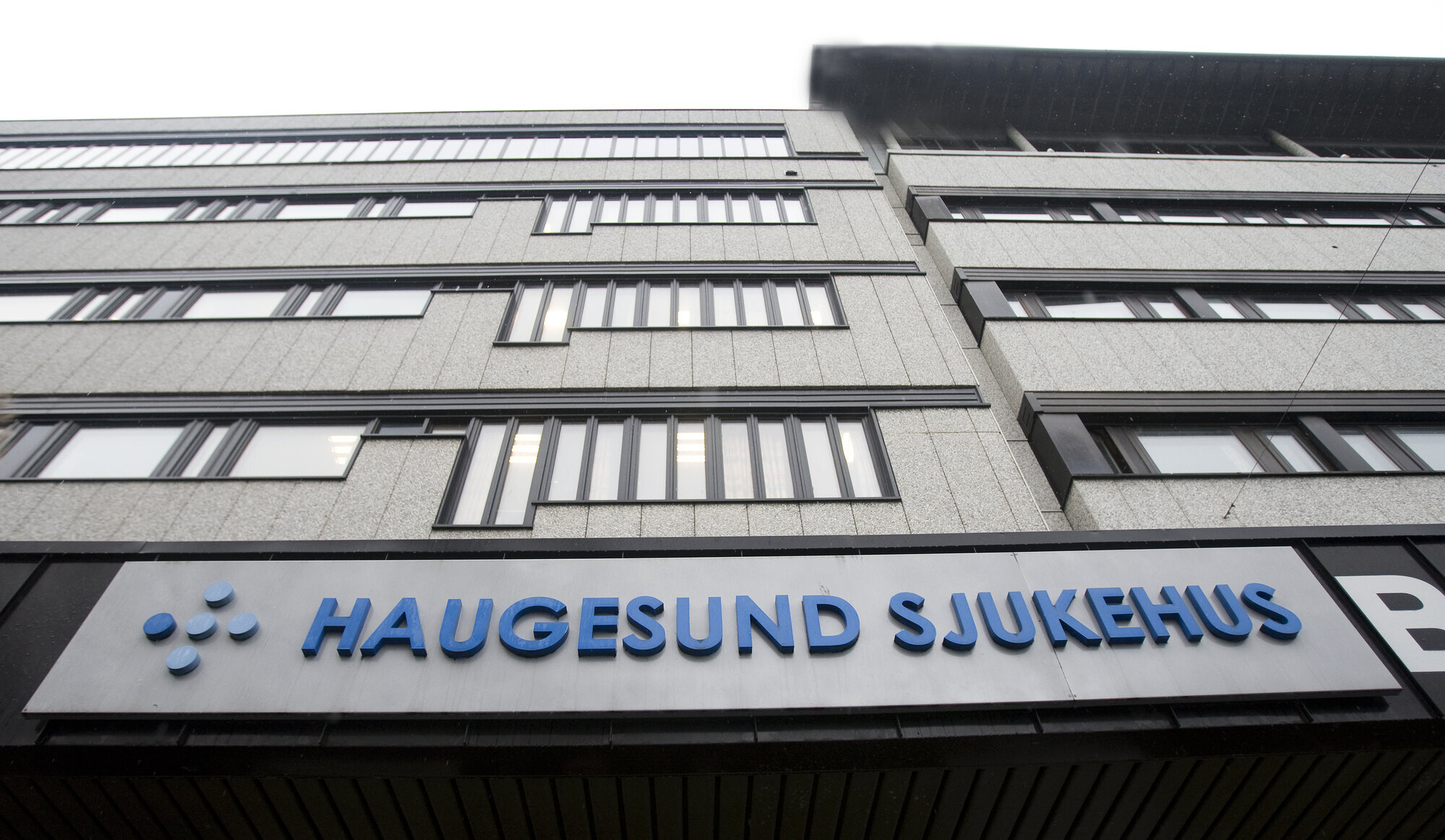 Grå fasade med blått skilt der det står Haukeland sjukehus