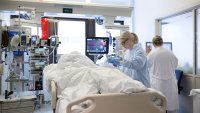 Intensivavdeling Bildet viser en intensivavdeling, der en pasient ligger i sengen mens en sykepleier står ved siden av. I bakgrunnen står legen og sjekker på en skjerm
