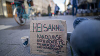Oslo Bildet viser Karl Johans gate og en plakat som en sittende mann har foran seg, hvor det er bønn om bidrag til en som har det vanskelig.