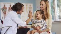 Mor og datter hos helsesykepleieren Bildet viser en liten datter på fanget til mora. Dattera gjør high five med en helsesykepleier som sitter overfor dem