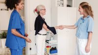 Konsultasjon Bildet viser en eldre kvinne som tar et helsepersonell i hånden mens at annet helsepersonell ser på