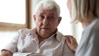 Mann med demenssykdom En kvinnelig sykepleier holder hånden på skulderen til en mann med demenssykdom