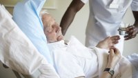 Sykepleier og pasient Bildet viser en eldre mann som får vann av en mannlig sykepleier.