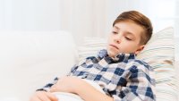 Barn Smerter Gutt med magesmerter som ligger på sofaen med et pledd over seg.