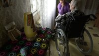 Hjemmesykepleie, eldreomsorg Bildet viser en eldre dame i rullestol sett bakfra og en yngre dame som sitter og lytter til henne.