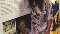 Hilde Helmine Leknes, fødselshistorier, Marie Treschow sykehjem Bildet viser Hilde Helmine Leknes som holder rundt en av historiene som er stilt ut, plakat på staffeli.