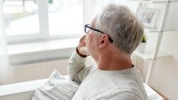 Lyst kledd middelaldrende mann sitter og ser ut av vindu. Hvitt lys.
