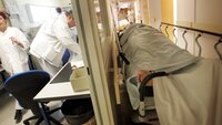 korridorpasient på sykehus Bildet viser korridorpasient på sykehus. Helsepersonell jobber i bakgrunnen