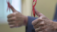 Verdens aidsdag, hiv, aids Bildet viser to hender med tomlene opp, dekorert med røy sløyfe.